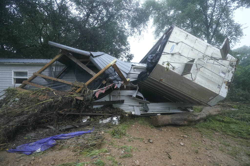 A mobile home and a truck trailer sit near a creek after being washed away from a storm