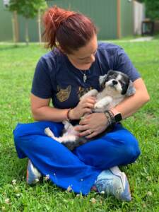 A person holds Gucci the pup in her arms while sitting on the grass outside