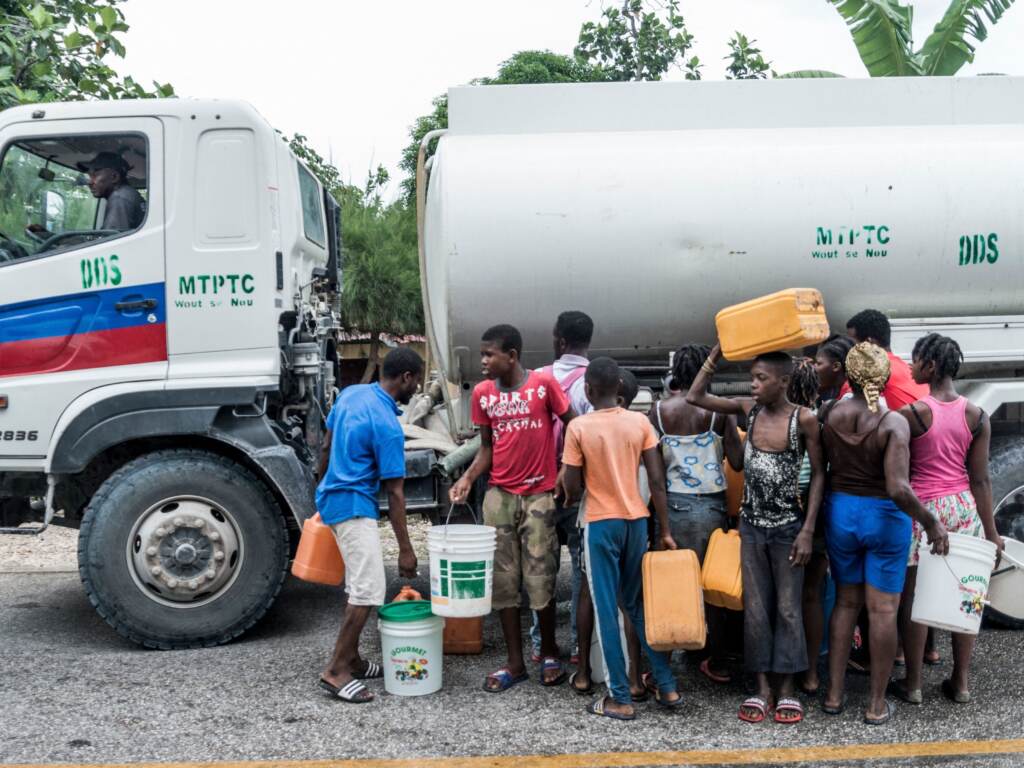 People gather near bins of water in Camp-Perrin, Haiti, on Monday. People gather near bins of water after the earthquake in Camp-Perrin
