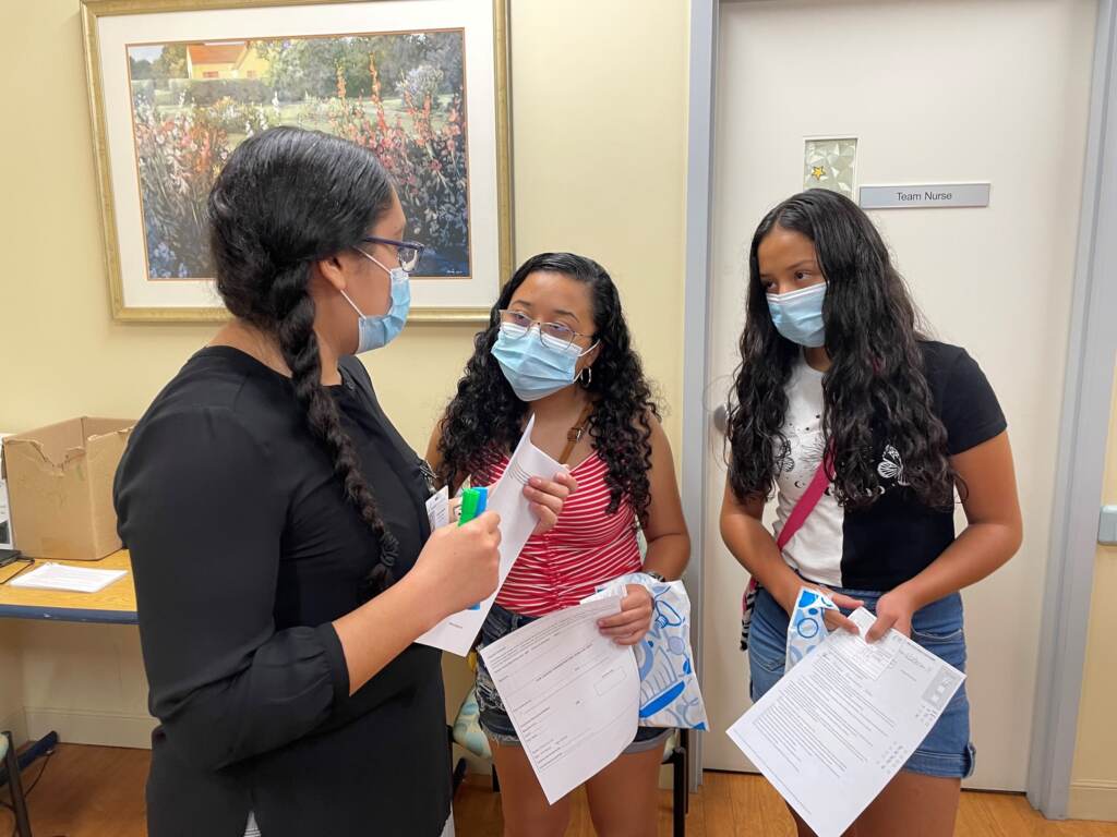 From left, Health Corps member Veronica Villalobos answers vaccine questions from teenagers Samantha and Fernanda Del Angel. (Cris Barrish/WHYY) 