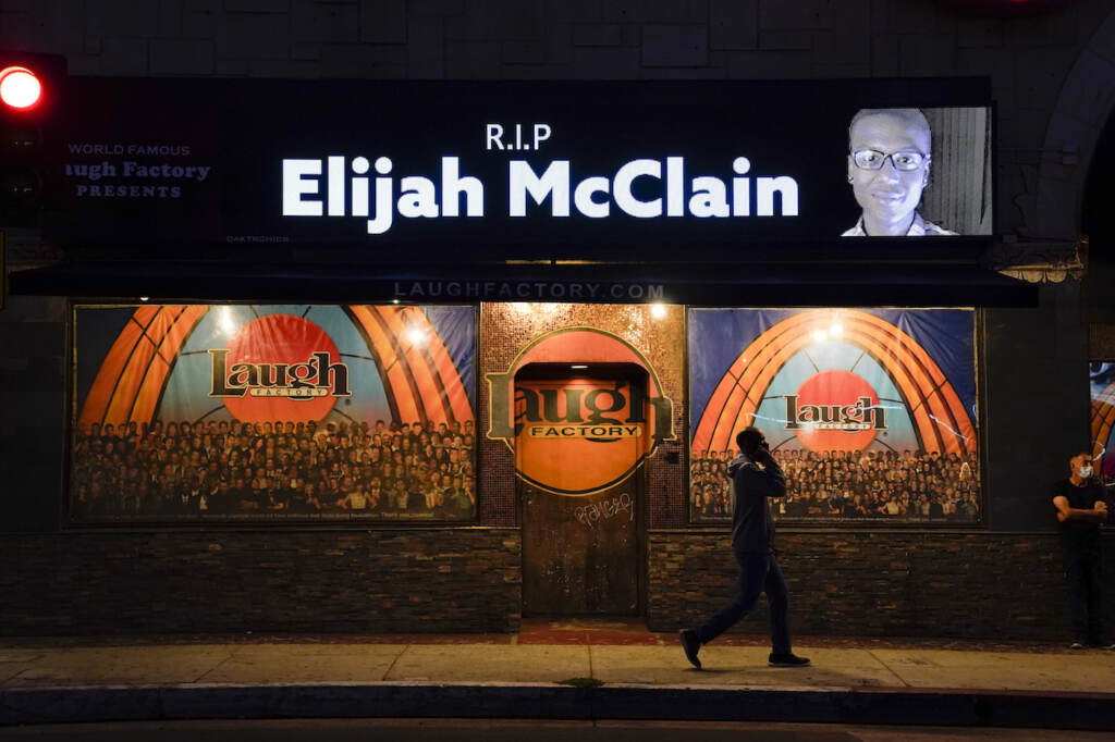 FILE - In this Aug. 24, 2020, file photo, a man walks past a display showing an image of Elijah McClain outside Laugh Factory during a candlelight vigil for McClain in Los Angeles.   Colorado’s attorney general said Wednesday, Sept. 1, 2021 that a grand jury indicted three officers and two paramedics in the death of Elijah McClain, a Black man who was put in a chokehold and injected with a powerful sedative two years ago in suburban Denver. (AP Photo/Jae C. Hong, File)