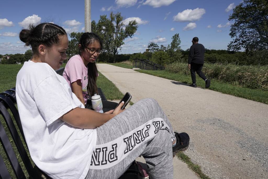 Virus Outbreak Spending Broadband Two girls sit on bench