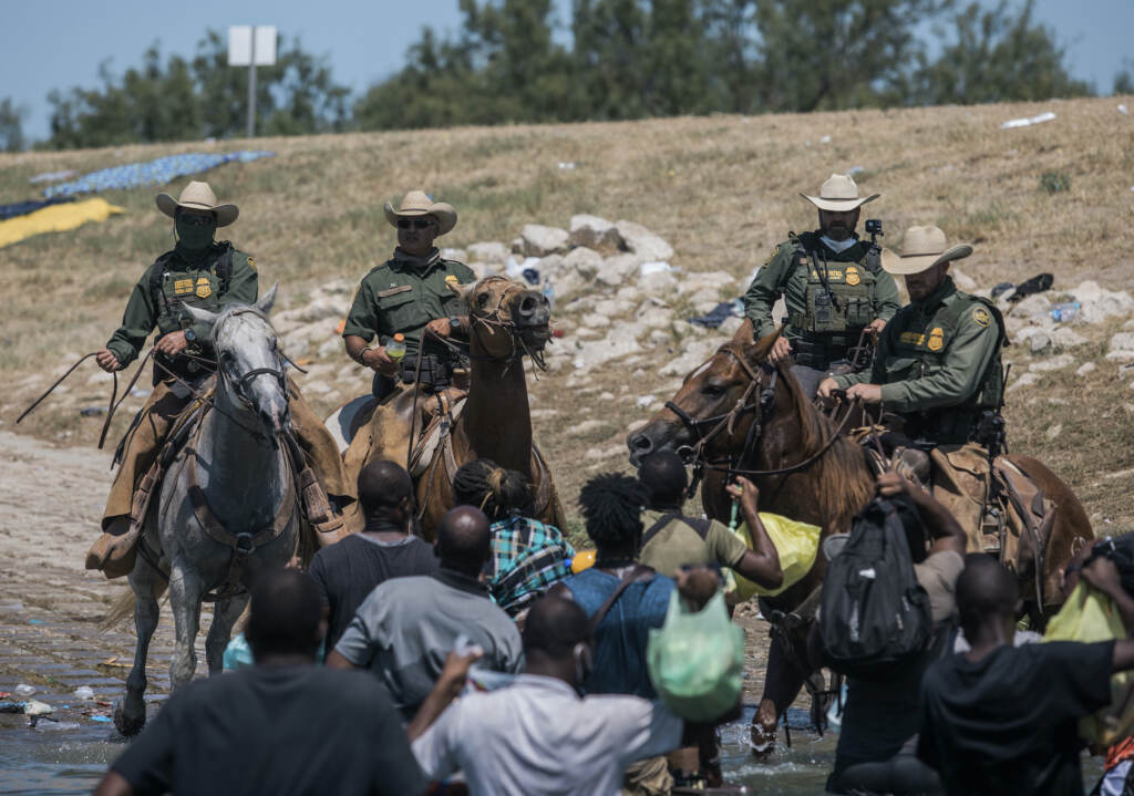 Mexico Border Migrant Camp U.S. border patrol officers are seen on horses, with Haitian migrants pictured crossing the Rio Grande below