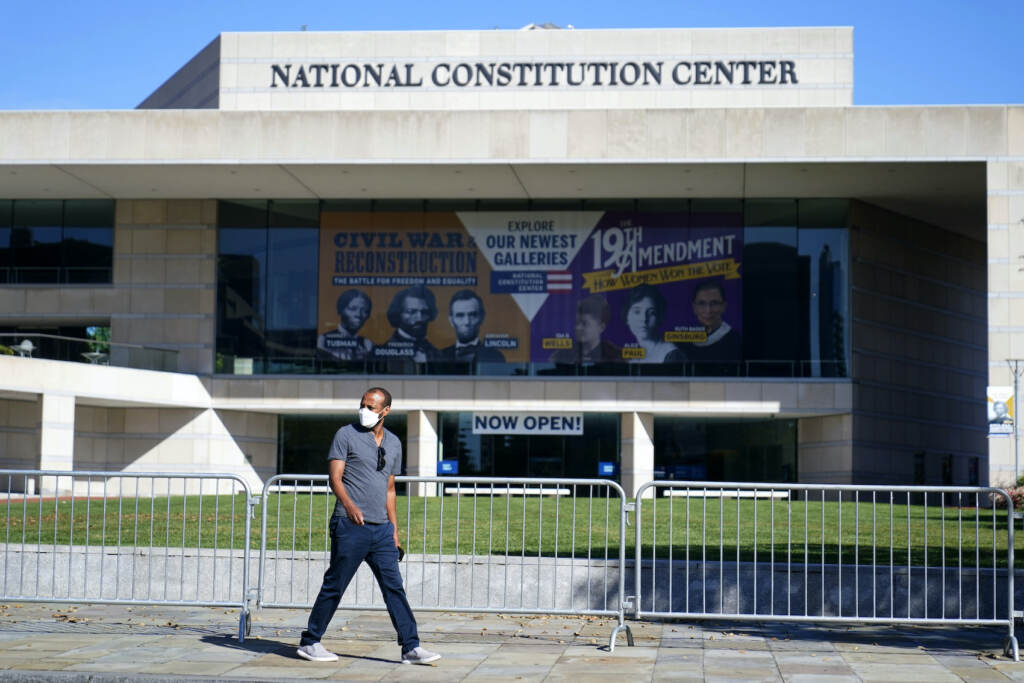 A man walks past the National Constitution Center while wearing a mask