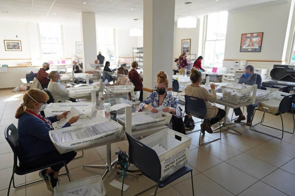 amistad_project_firm_election_2020_091121 People sit at tables in a room with ballots from the 2020 election
