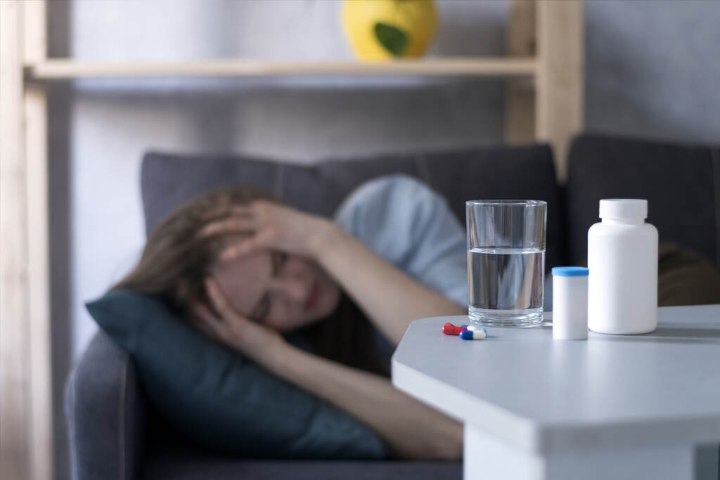 Woman Lies On Couch And Suffers From Migraine. Bottles With Pill Woman Lies On Couch