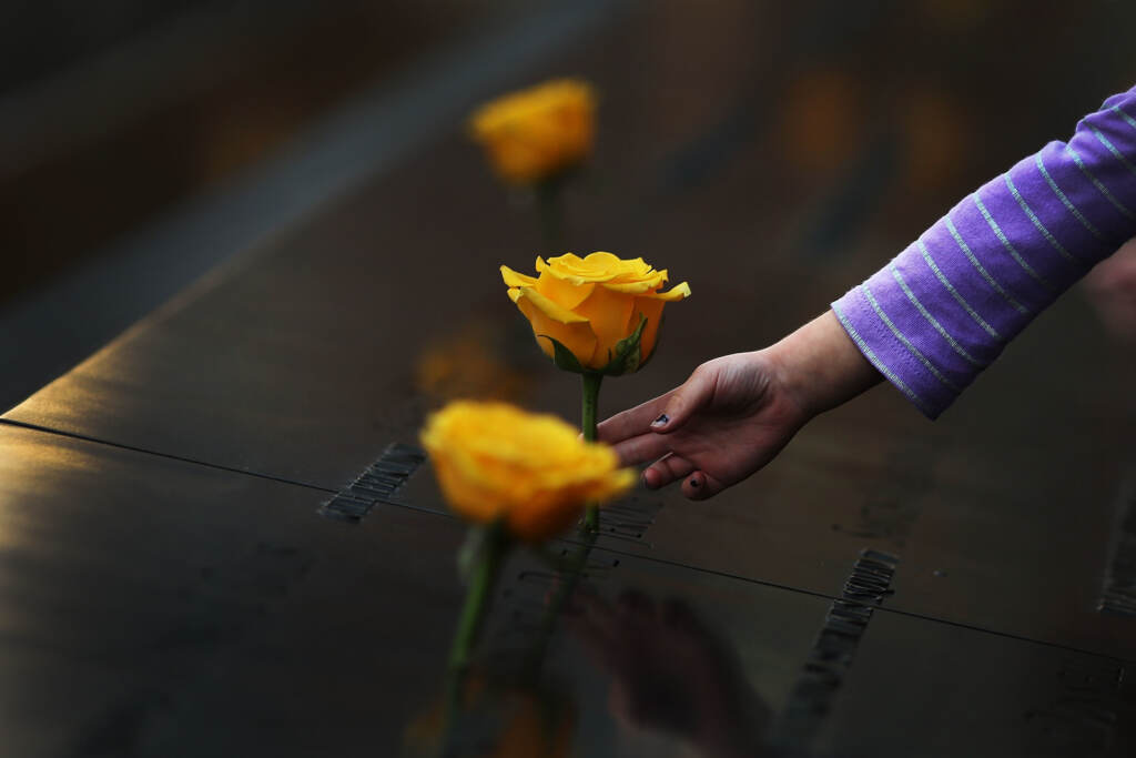 A child reaches out to touch a flower adorning the Sept. 11 memorial on the name of a veteran killed in the 2001 terror attacks. For today’s generation of kids, 9/11 is a history lesson.