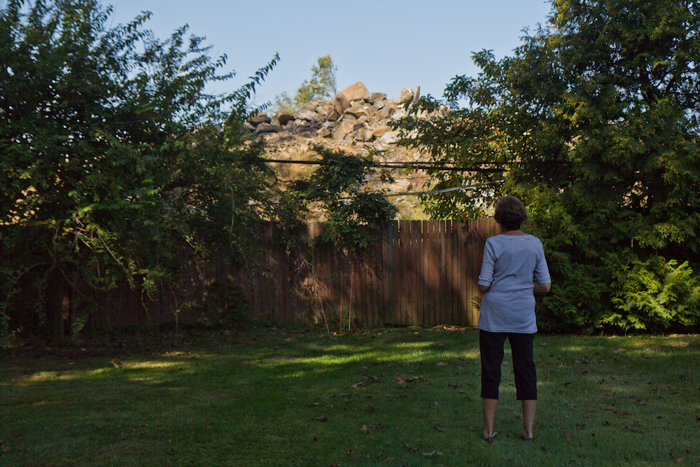 Resident Ann Gelfond stands in front of a pile of rubble behind her yard. She pointed to disturbances she’s experienced for the past few three years of construction of the Lower Merion School District’s new middle school taking place behind her house, as an indication of what the construction of athletic fields in the neighborhood would be like. (Kimberly Paynter/WHYY)
