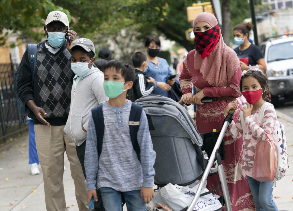 Virus Outbreak Parents stand with their kids outside, all while wearing face masks