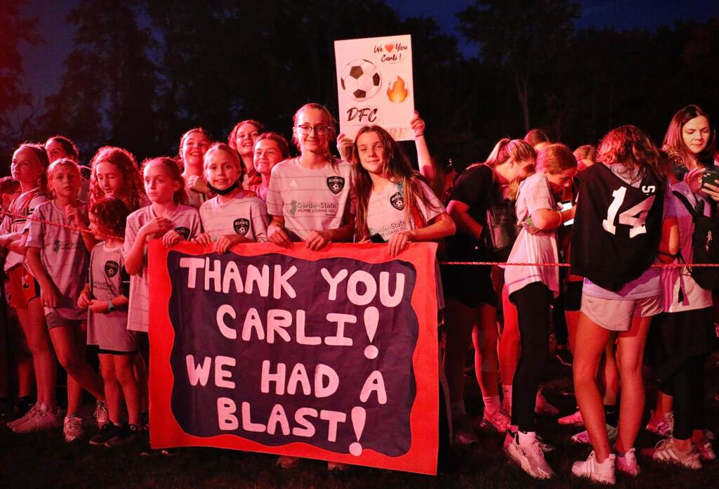 Members of the Delran Football Club carry a banner for Carli Lloyd in the glow from a video monitor