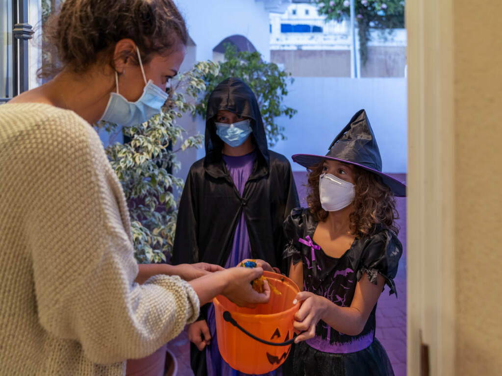 Children Dressed In Halloween Costumes Trick-Or-Treating In COVID-19 Times Children dressed in halloween costumes, while wearing face masks, trick-or-treating