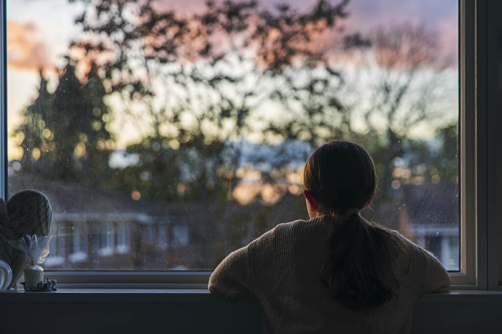 A girl looks out of her bedroom window as the sun is setting