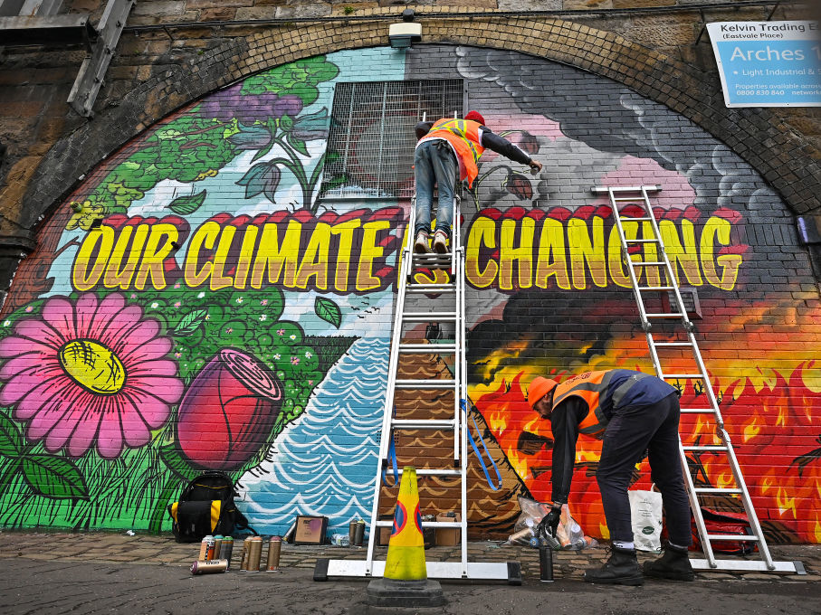 Artists paint a mural on a a wall next to the Clydeside Expressway that reads 