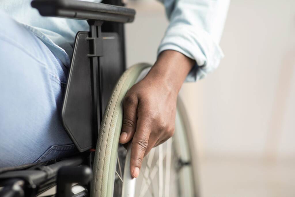 Man controlling equipment, health care in clinic and support of invalid human Man controlling equipment, health care in clinic and support of invalid human. Middle aged african american male disabled in wheelchair. Selective focus on hand on wheel, close up, cropped, free space
