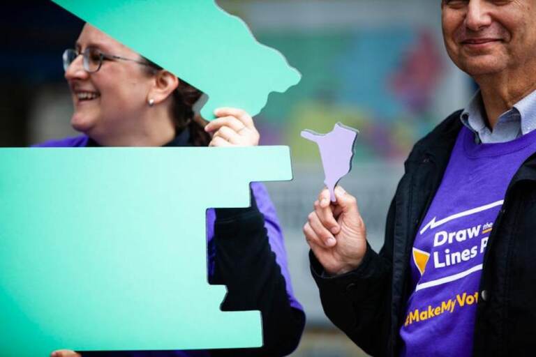 Members of the Draw the Lines initiative stand with cutouts of congressional districts at a Capitol protest