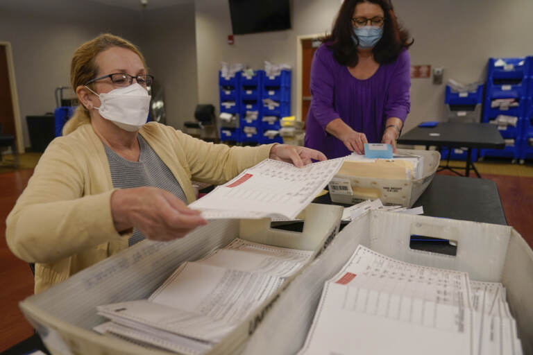 Board worker Ann Carlette, left, process and double-check mail-in ballots