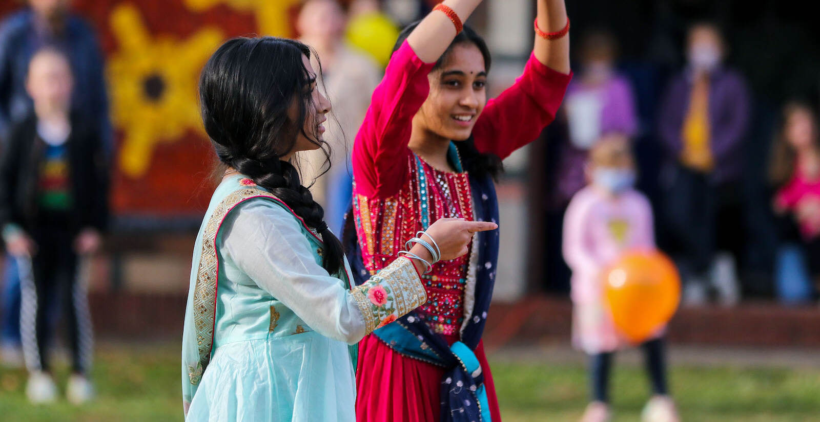 Two people dancing, dressed in colorful saris, during a Diwali celebration.