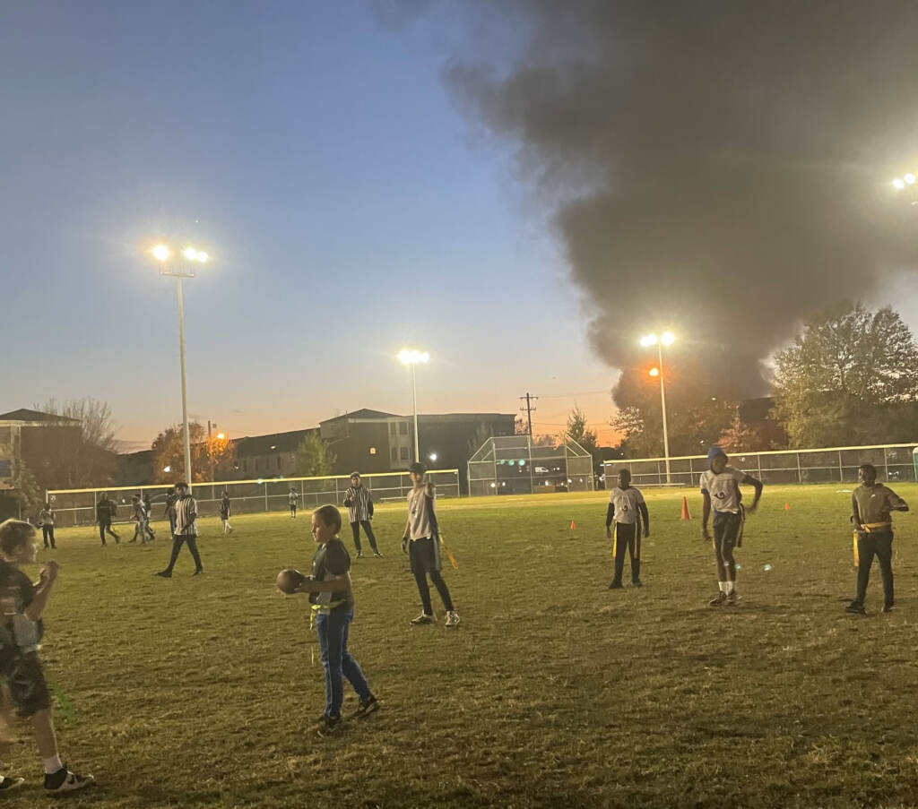 Young people play football at Lanier Park on Tuesday after a junkyard fire sent smoke into the air. (Photo provided by Alexandre Imbot ) Young people play football at Lanier Park on Tuesday after a junkyard fire sent smoke into the air.