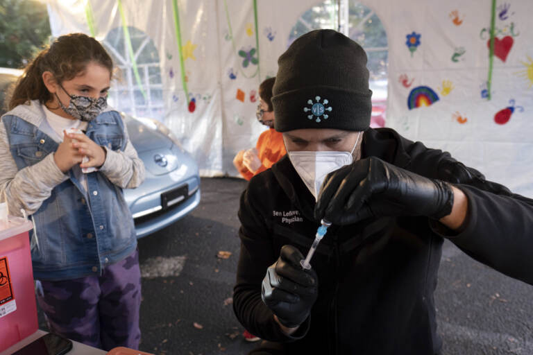 Leah Lefkove, 9, waits as her dad Dr. Ben Lefkove prepares the first COVID-19 vaccine for her at the Viral Solutions vaccination and testing site in Decatur, Ga., on the first day COVID-19 vaccinations were available for children from 5 to 12 on Wednesday, Nov. 3, 2021. The U.S. enters a new phase Wednesday in its COVID-19 vaccination campaign, with shots now available to millions of elementary-age children in what health officials hailed as a major breakthrough after more than 18 months of illness, hospitalizations, deaths and disrupted education. (AP Photo/Ben Gray)