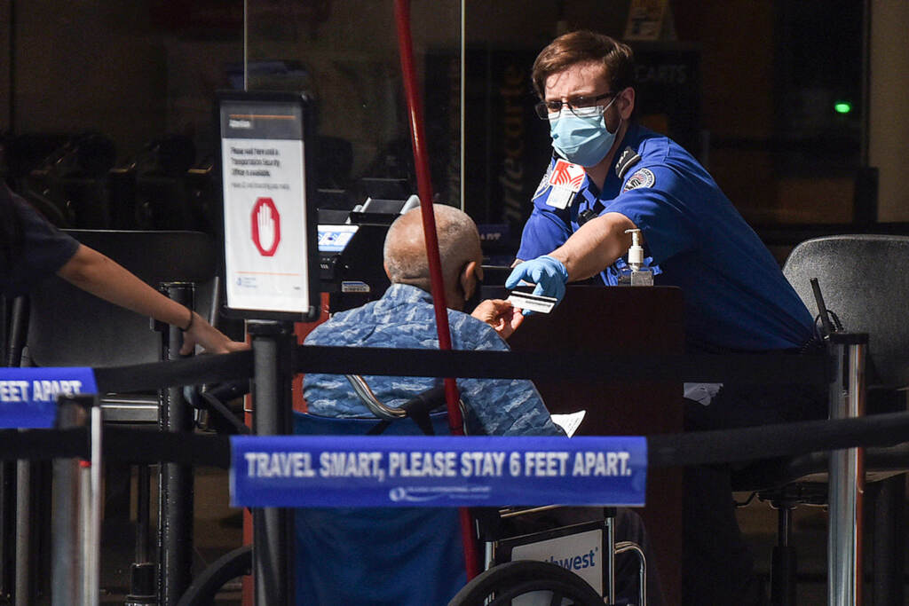A man using a wheelchair hands his ID to an officer at a security screening checkpoint at Orlando International Airport in 2020. A man in a wheelchair hands his ID to a TSA officer