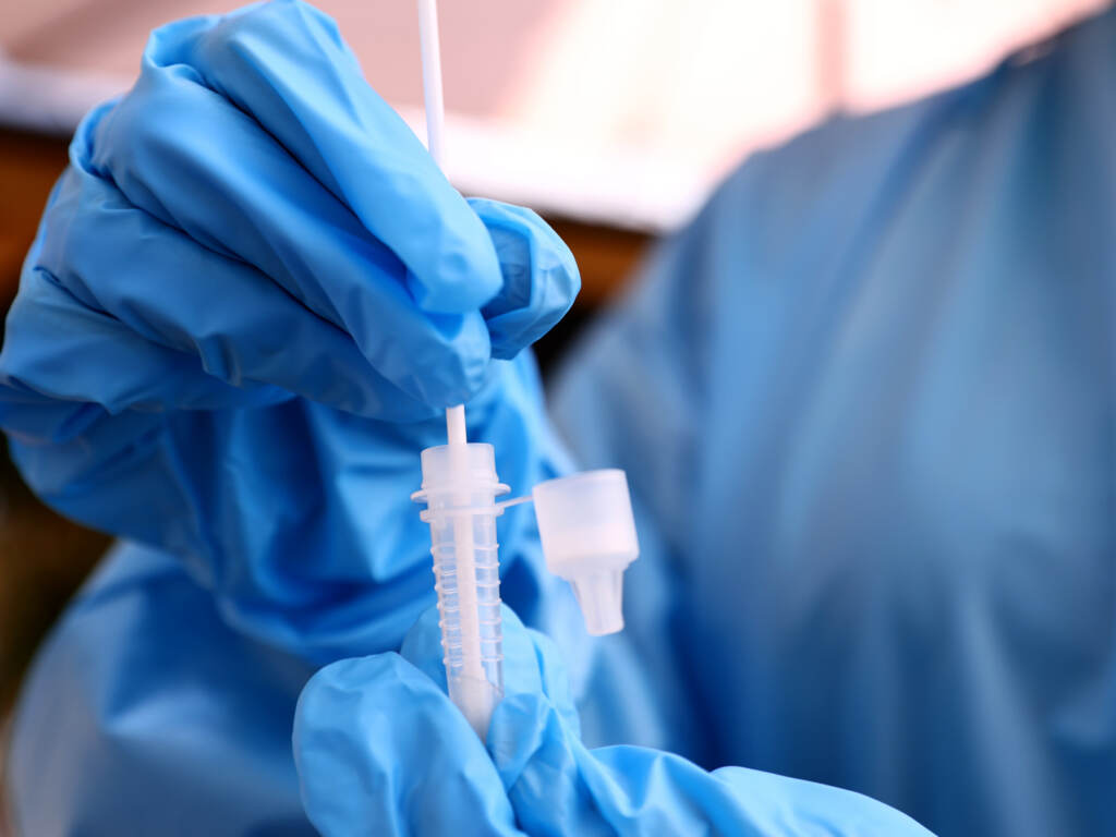 A registered nurse stirs a nasal swab in testing solution after administering a COVID-19 test in Los Angeles, Calif. Increased testing could help in efforts to detect and track new variants like omicron. A registered nurse stirs a nasal swab in testing solution