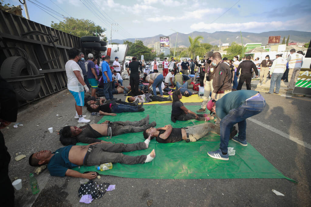 Injured migrants are cared for on the side of the road next to the overturned truck on which they were traveling near Tuxtla Gutierrez, Chiapas state, Mexico, Dec. 9, 2021. Mexican authorities say at least 49 people were killed and dozens more injured when the truck carrying the migrants rolled over on the highway in southern Mexico