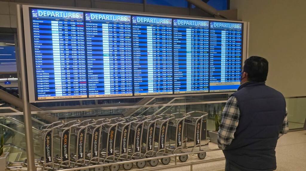 A man looks at the departures board at Salt Lake City International Airport Friday, Dec. 24, 2021, in Salt Lake City. At least three major airlines say they have canceled dozens of flights because illnesses largely tied to the omicron variant of COVID-19 have taken a toll on flight crew numbers during the busy holiday travel season.