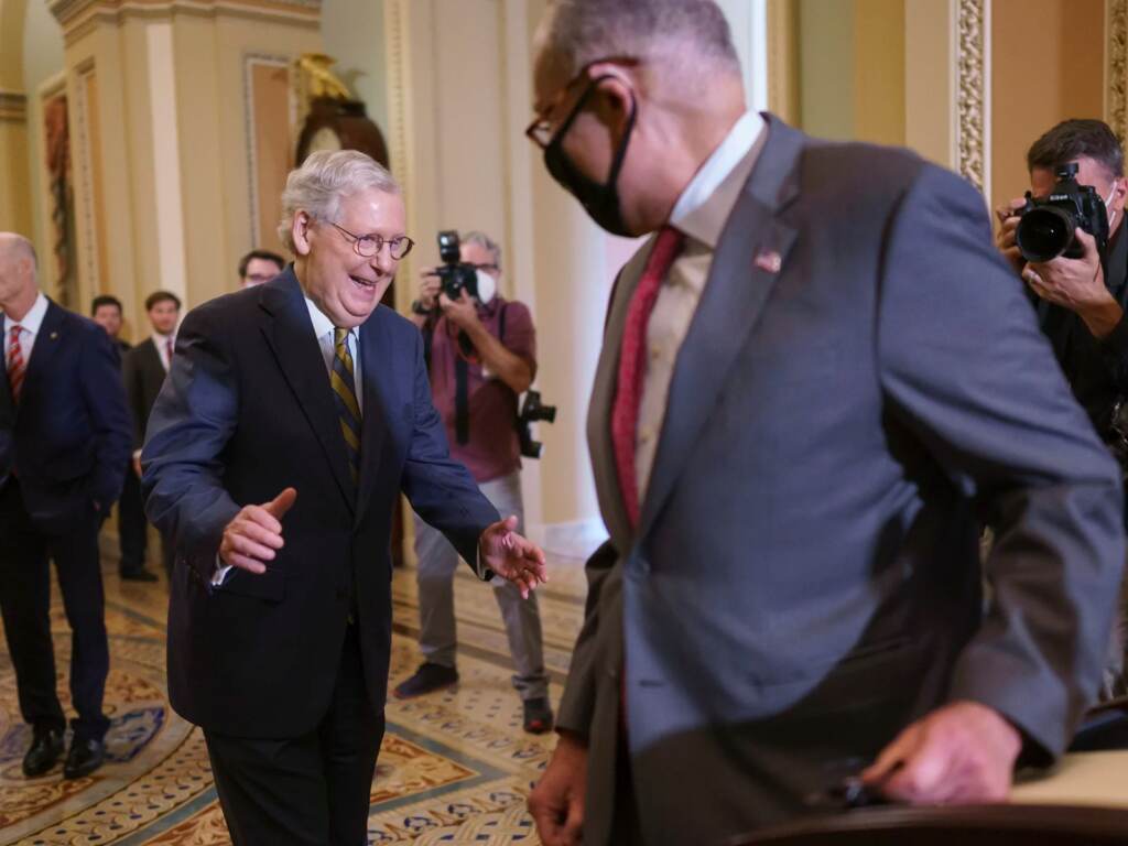 Senate Minority Leader Mitch McConnell, R-Ky., and Senate Majority Leader Chuck Schumer, D-N.Y., have agreed on a plan to try to avoid a federal default without GOP votes. In this Aug. 3, 2021, photo, Senate Democratic Leader Chuck Schumer, of New York, and Senate Republican Leader Mitch McConnell, of Kentucky, left rear, smile when they both arrived at the same time to speak to reporters about progress on infrastructure bill, at the Capitol in Washington. Senators are convening for a rare weekend session on the bipartisan infrastructure bill as they edge toward a vote. Saturday's action in the Senate could wrap up swiftly with passage of the $1 trillion package or drag out for days by opponents trying to slow President Joe Biden’s big priority.