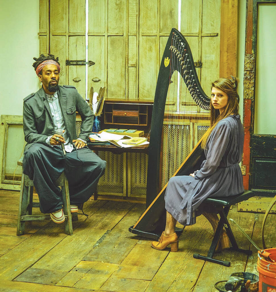 kuf-knotz-christine-elise-music-123021 Kuf Knotz sits while holding a mic, as Christine sits next to her harp