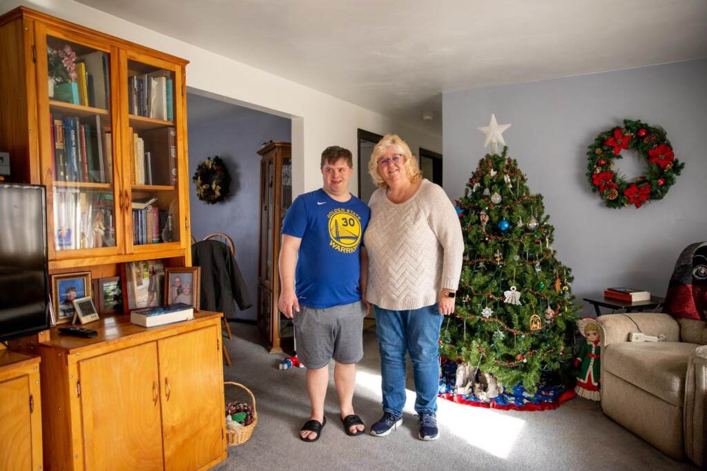 Lisa Stagon and her son Chris smile for a photo in front of a Christmas tree