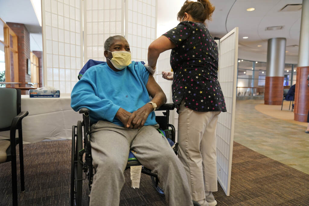 Virus Outbreak Nursing Homes Edward Williams, 62, a resident at the Hebrew Home at Riverdale, receives a COVID-19 booster shot in New York, Sept. 27, 2021. COVID-19 infections are soaring again at U.S. nursing homes because of the omicron wave, and deaths are climbing too. That's leading to new restrictions on family visits and a renewed push to get more residents and staff members vaccinated and boosted. (AP Photo/Seth Wenig, File)
