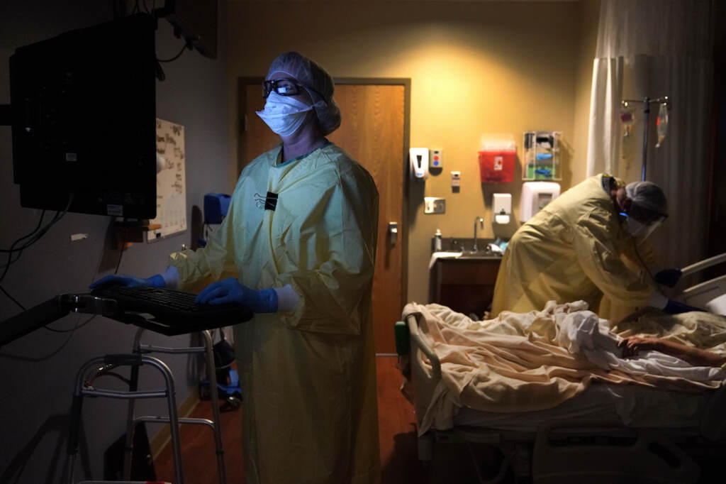 Registered nurse Shelly Girardin, left, is illuminated by the glow of a computer monitor as Dr. Shane Wilson examines COVID-19 patient Neva Azinger inside Scotland County Hospital in Memphis, Mo., on Nov. 24, 2020. (AP Photo/Jeff Roberson, File)
