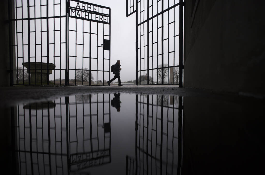 A person walks behind the gate of the Sachsenhausen Nazi death camp with the phrase 'Arbeit macht frei' (work sets you free) in Oranienburg, about 30 kilometers (18 miles) north of Berlin, Germany, Tuesday, Jan. 25, 2022. On Thursday Jan. 27, 2022 the International Holocaust Remembrance Day marks the liberation of the Auschwitz Nazi death camp on Jan. 27, 1945. (AP Photo/Markus Schreiber)