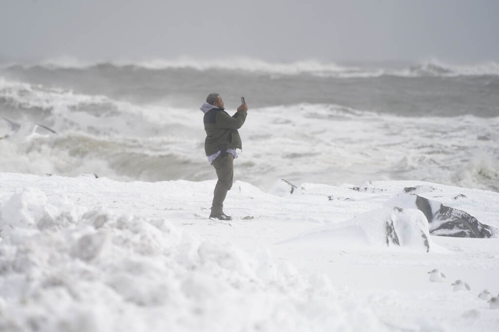 Winter Weather Maryland Waves crash behind a man as he uses a cell phone to capture images on a snow-covered beach, Saturday, Jan. 29, 2022.(AP Photo/Julio Cortez)