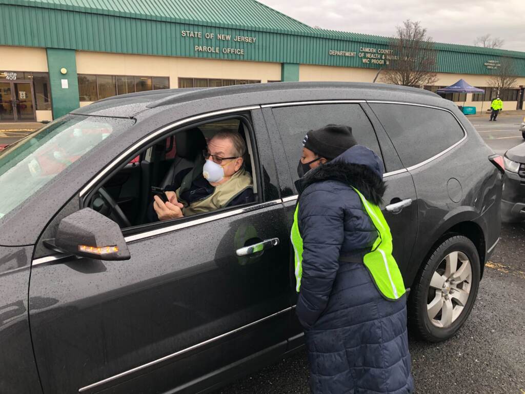 Image from iOS (22) Koren Norwood, a Camden County health educator, assists Steve Shirk, of Audobon, with the COVID test packet, which includes a QR code to get to the website. Shirk was one of dozens to arrive to a new drive-in COVID testing site in Camden on Jan. 5, 2022. (P. Kenneth Burns/WHYY)