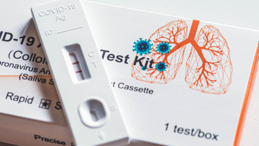YOK-1-28-bigstock-Positive-Covid–Antigen-Test-437628092 A close up of a positive Covid-19 antigen test kit and box with an illustration of lungs and a virus particle