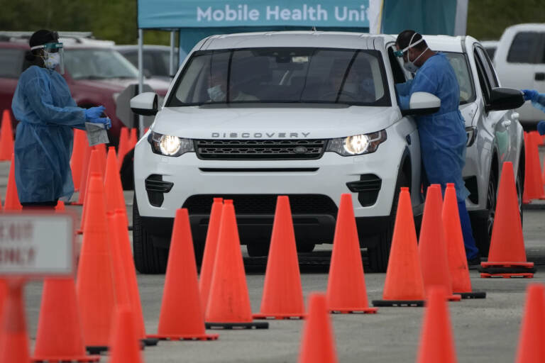 Health care workers administer nasal swabs to drivers and passengers at a drive-thru COVID-19 testing site