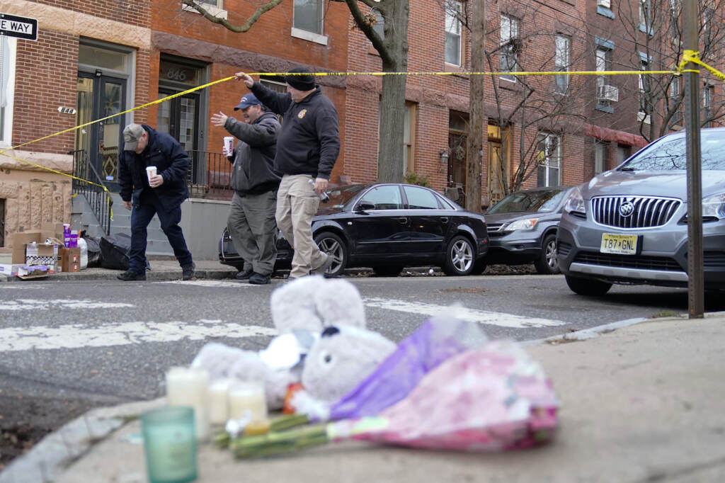 Officials pass flowers and other items left in memory of victims of a fatal fire