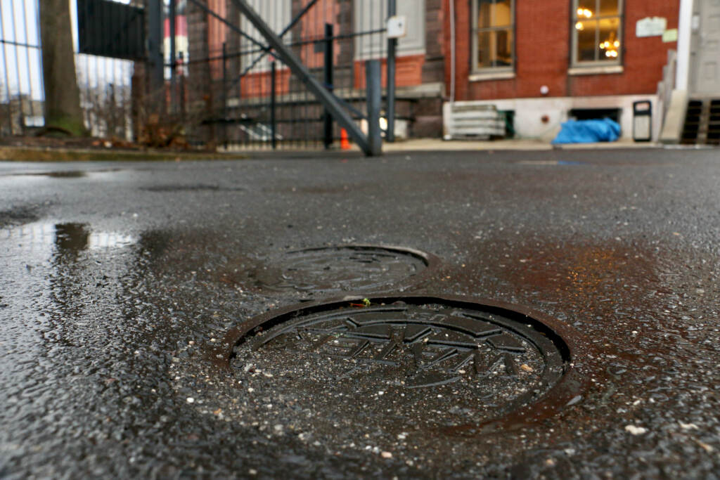 2022 02 07=e lee-phioladelphia german american society-geothermal wells Metal caps marked ''WATER'' are the only evidence of the 400-foot wells beneath the parking lot of the German Society of Pennsylvania on Spring Garden Street. The wells tap the geothermal energy of the earth to heat and cool the society's building. (Emma Lee/WHYY)