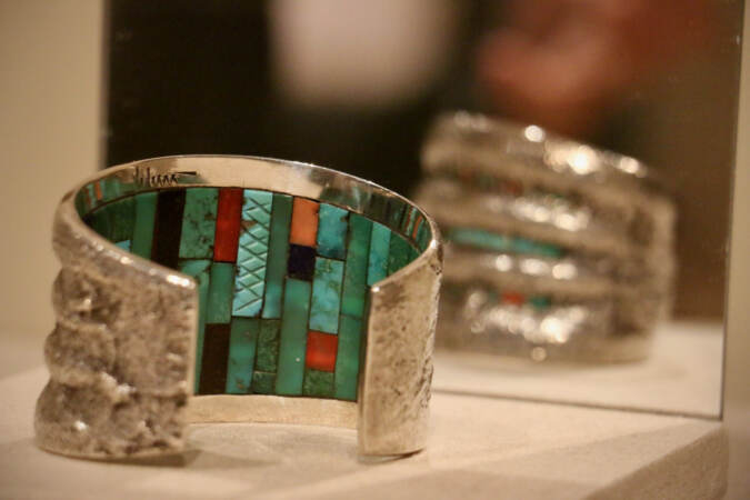 A silver bracelet by Hopi artist Charles Loloma is lined on the inner side only with a patern of turquoise, coral, wood, malachite, and lapis lazuli. (Emma Lee/WHYY)