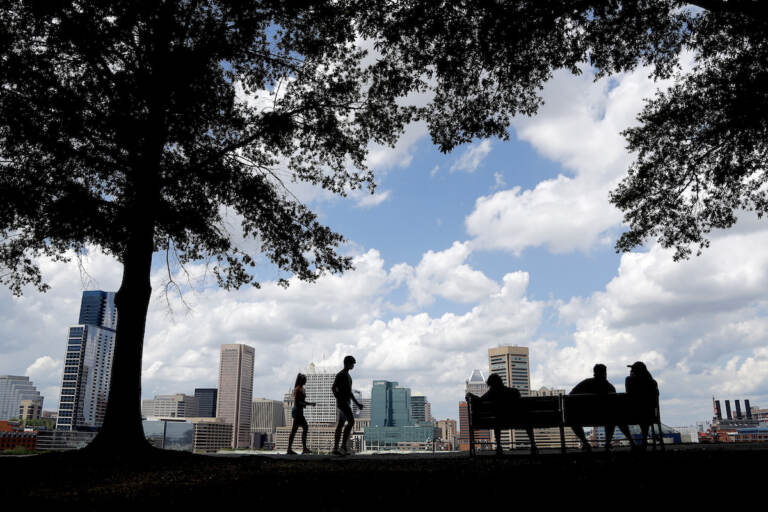 The Baltimore skyline is seen at a distance as people enjoy a warm day, Wednesday, July 1, 2020, in the Federal Hill neighborhood of Baltimore. (AP Photo/Julio Cortez)