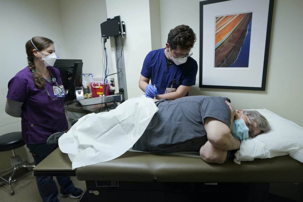 Ray Hoffman is given a shot while laying down in a medical facility