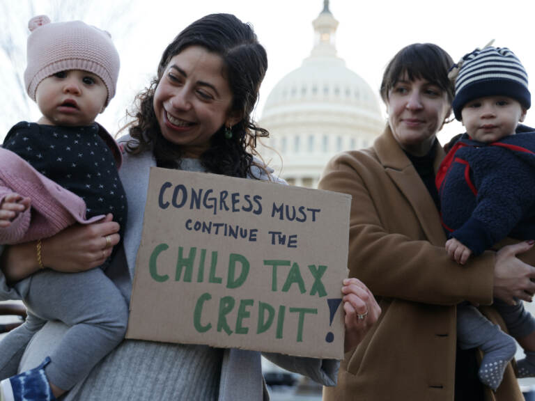 Two parents, each holding up children, stand in front of a sign that says, 