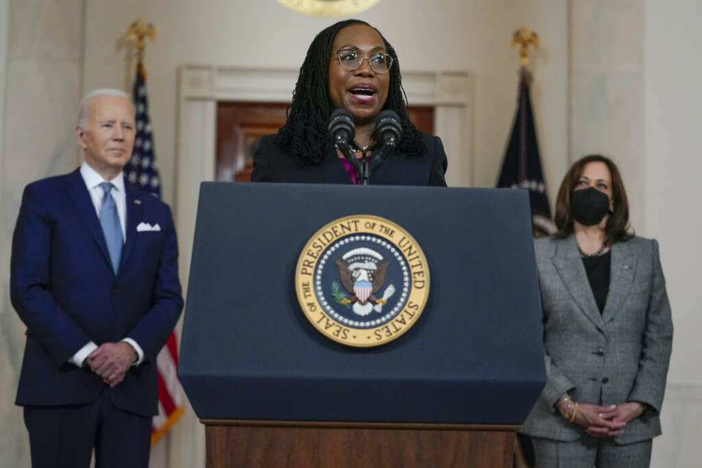 Joe Biden Judge Ketanji Brown Jackson speaks from a podium, with President Biden to her right and Vice President Harris to her left