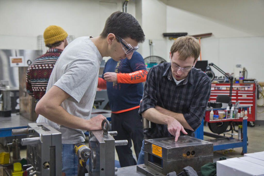 2022 03 10 kpaynter mitch engleka and nick ball southco manufacturing Mitch Engleka, 28, manufacturing engineer (right) and Nick Ball, a manufacturing technician (left), inspect a mold that creates latches to secure the spare tire on a Dodge Durango at Southco in Concordville, Pa.(Kimberly Paynter/WHYY)