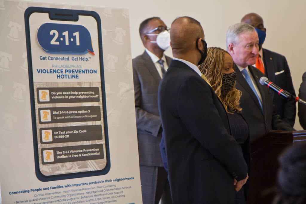 2022 03 28 mayor kenney 211 A sign announcing the gun violence prevention hotline is shown in the foreground, with elected officials speaking at a podium in the background.