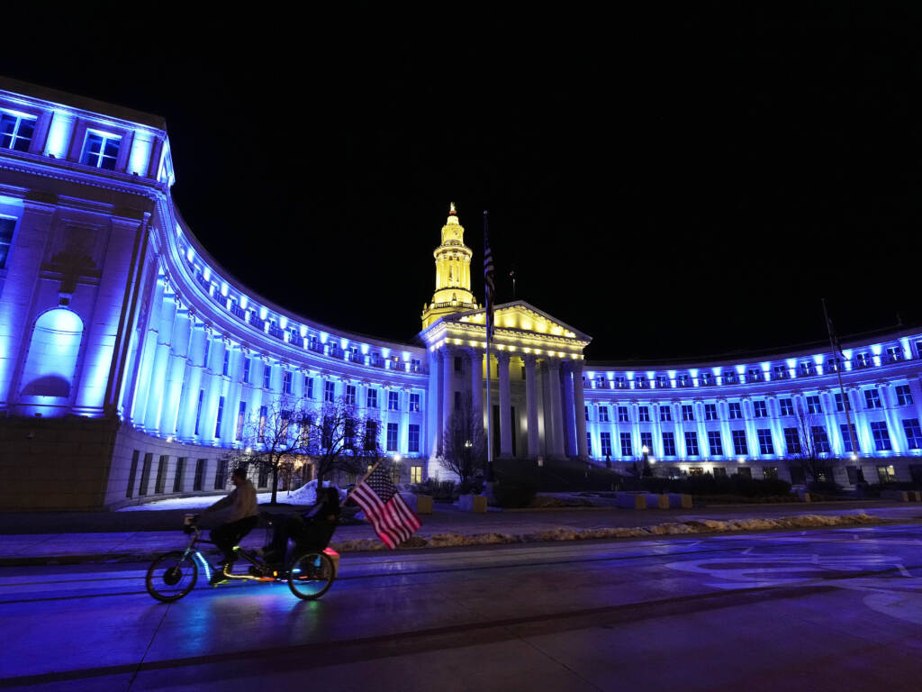 An American flag unfurls off a pedicab as it glides past the Denver City/County Building, which is illuminated in yellow and blue in support of Ukraine on Monday. Colorado’s State Capitol will also be illuminated in blue and yellow in support of Ukraine. An American flag unfurls off a pedicab as it glides past the Denver City/County Building, which is illuminated in yellow and blue in support of Ukraine, late Monday, Feb. 28, 2022, in Denver. (AP Photo/David Zalubowski)