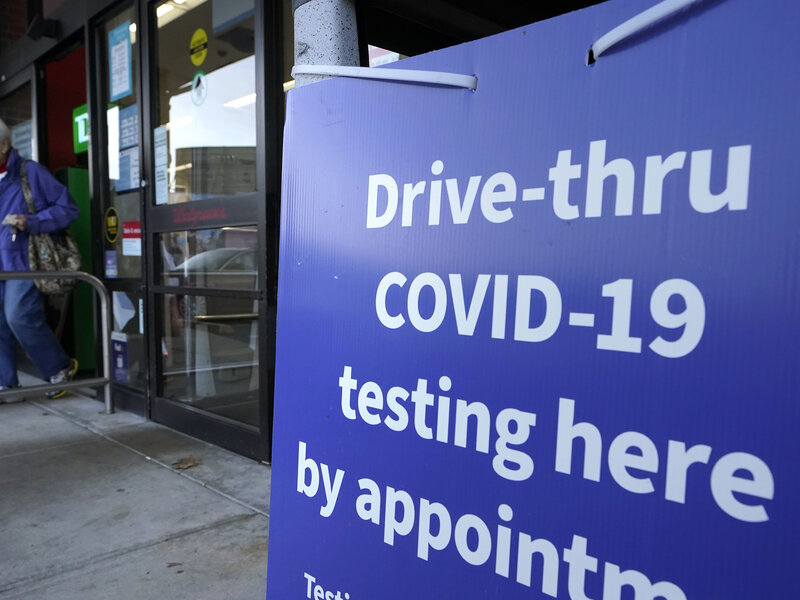 Virus Outbreak Massachusetts A passer-by walks past a sign that calls attention to COVID-19 testing while departing a Walgreens pharmacy