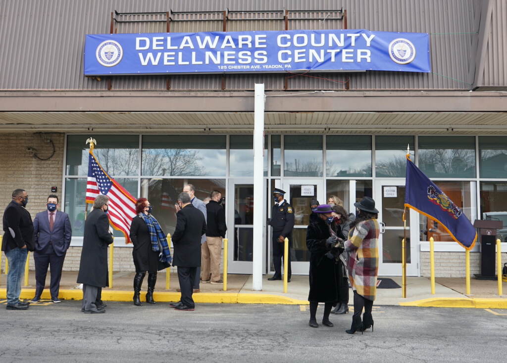 delco_wellness_center_KC_021021_01 People stand outside of a building with a banner that reads,
