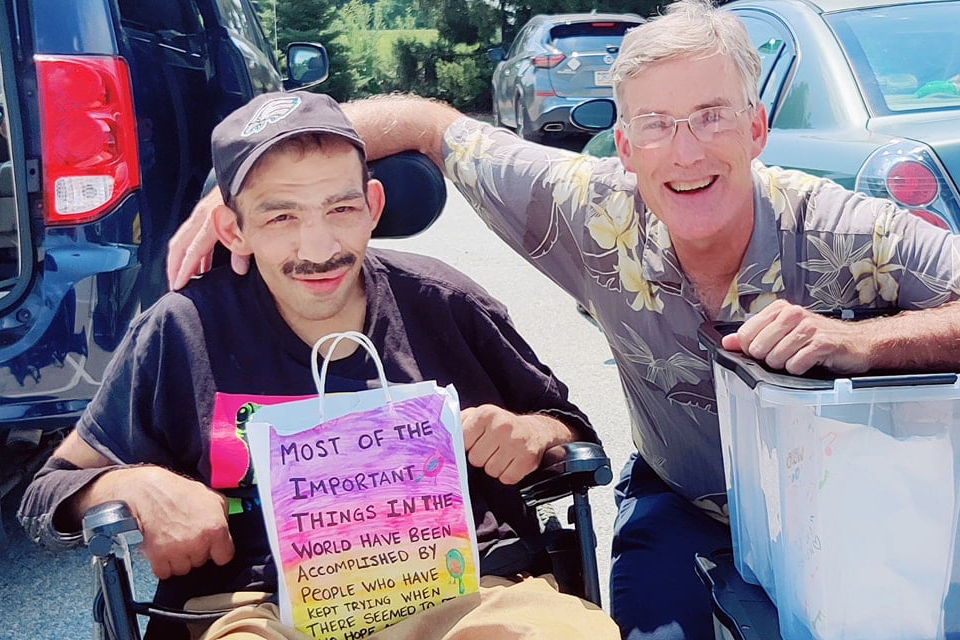 Steven Abi Richa (left) holding a decorated paper bag filled with household items next to Chris Batton (right)